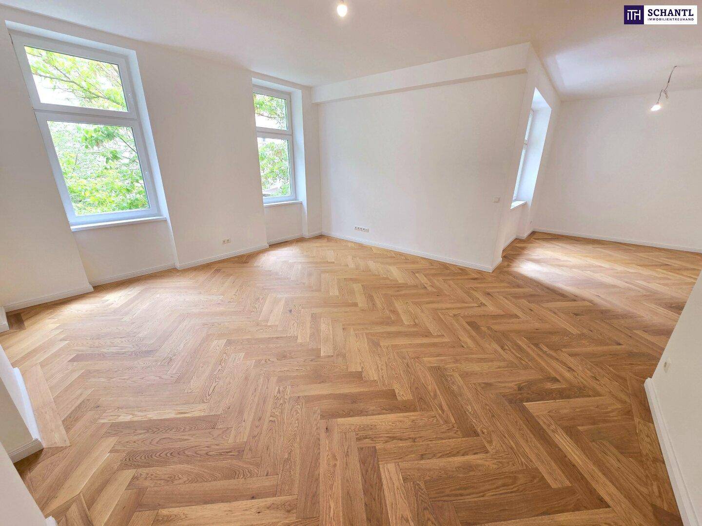 Großzügiges Zimmer mit Fischgrätparkett und vielen Fenstern, die für eine helle Atmosphäre sorgen.