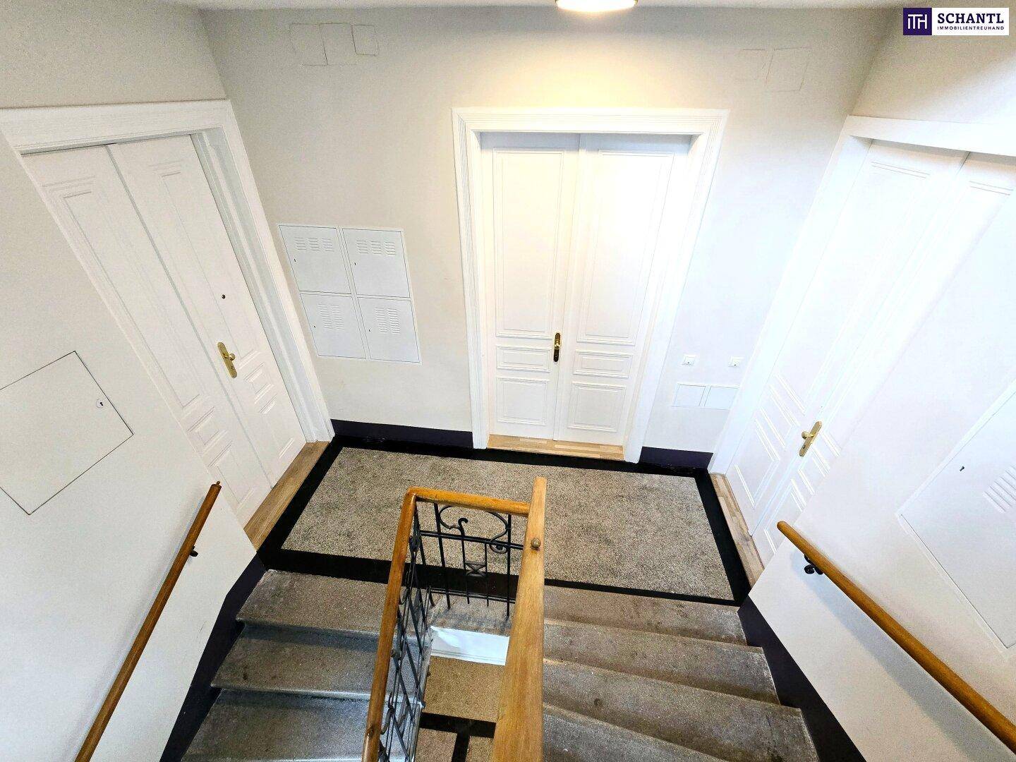 Treppenhaus-Podest mit Teppichläufer und mehreren Eingangstüren, von oben betrachtet.