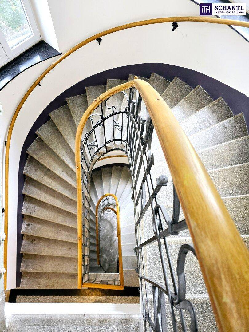Elegante Wendeltreppe mit schmiedeeisernem Geländer und Holzhandlauf in einem historischen Gebäude.