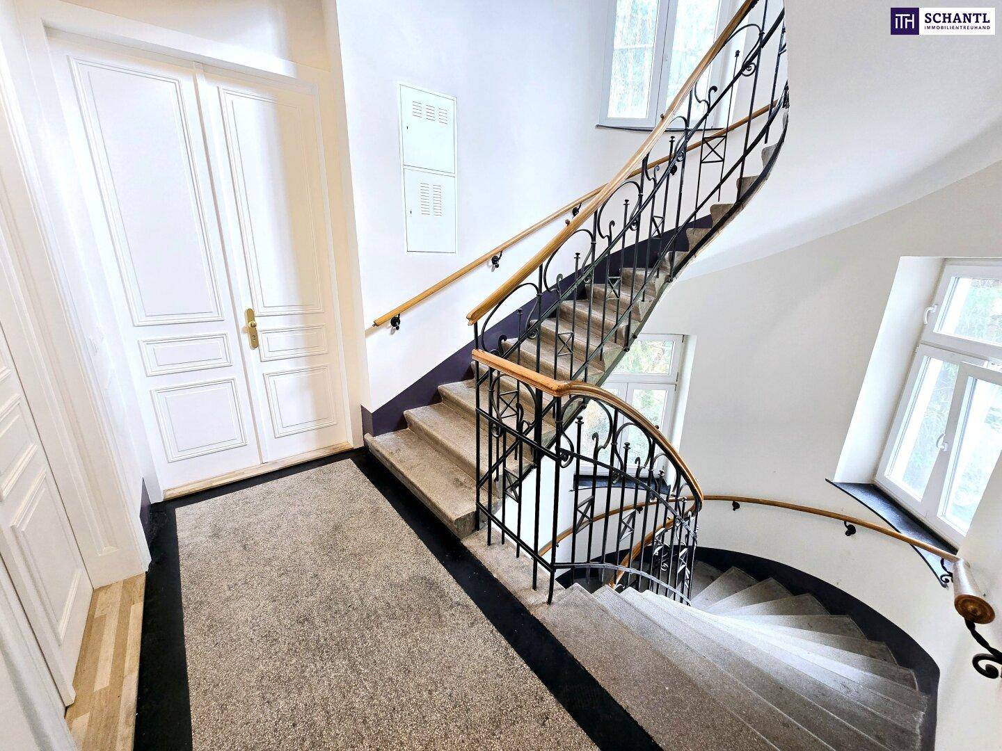 Repräsentatives Treppenhaus mit geschwungener Treppe, schmiedeeisernem Geländer und Teppichläufer.