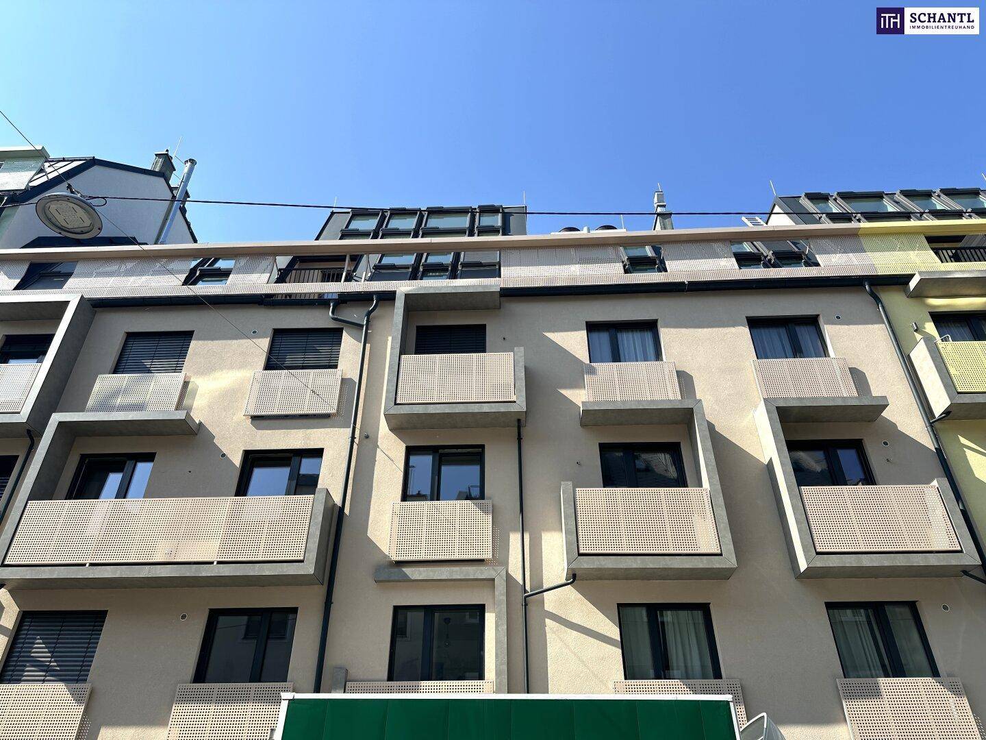 Ansicht eines modernen Apartmentgebäudes mit beiger Fassade, Balkonen und großen Fenstern.