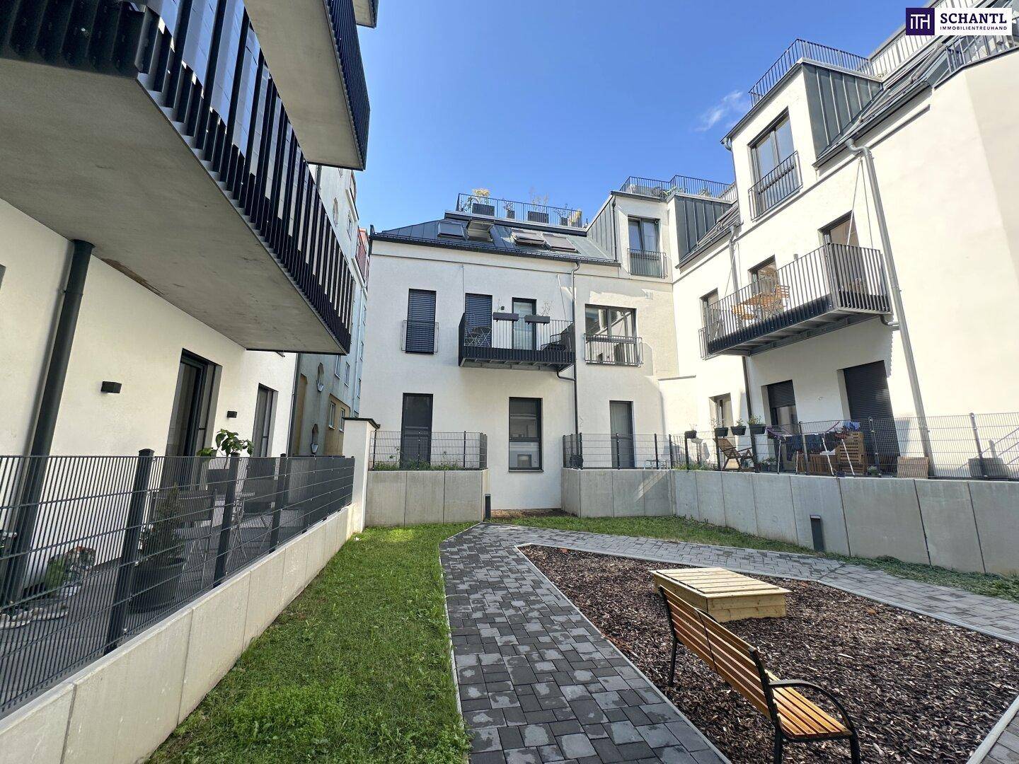 Moderner Apartmentkomplex mit weißer Fassade, Balkonen und einem gemeinschaftlichen Gartenbereich mit Sitzbank.