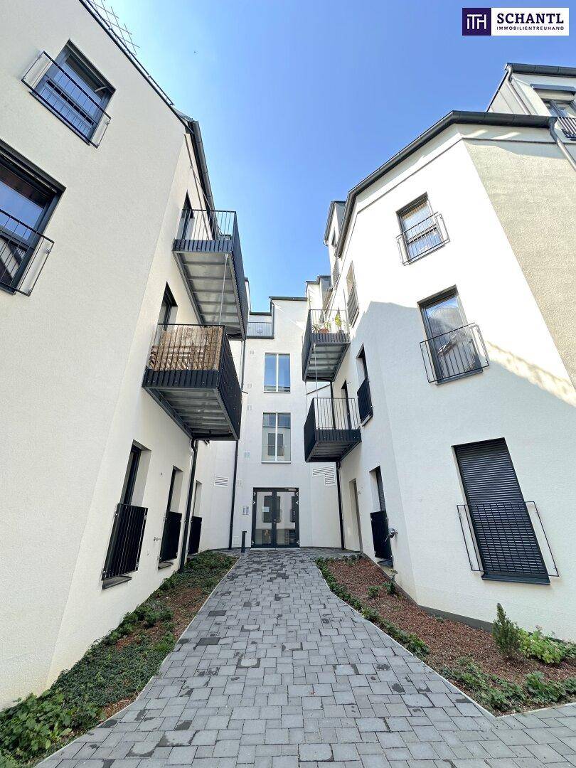 Weg zwischen zwei modernen Apartmentgebäuden mit weißen Fassaden und Balkonen unter blauem Himmel.
