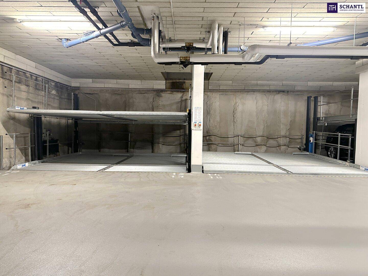 Tiefgarage mit modernen Parkliftsystemen und sichtbaren Versorgungsleitungen an der Decke.