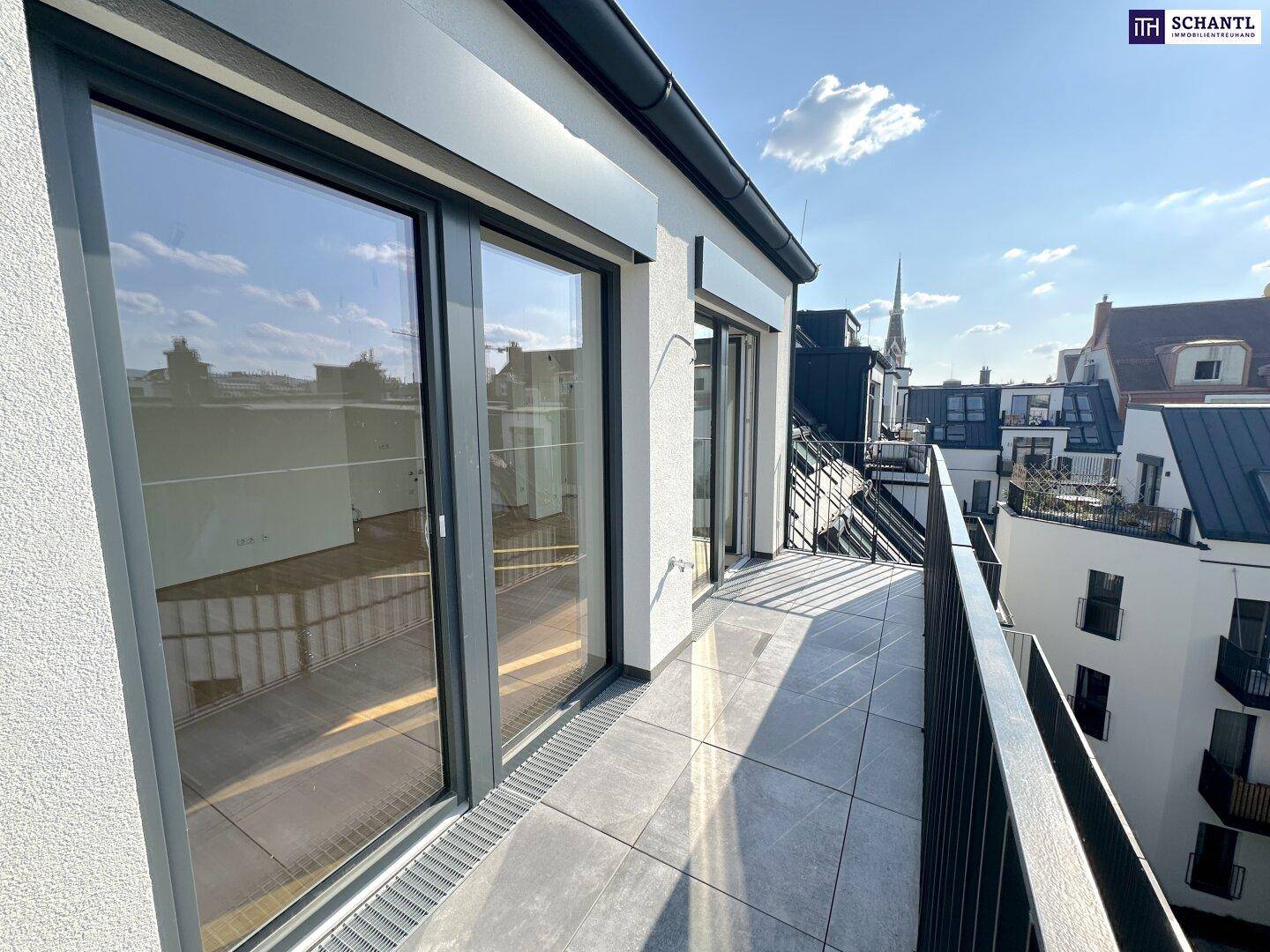 Großer Balkon mit Fliesenboden und Metallgeländer, bietet einen weiten Blick über die Dächer der Stadt.