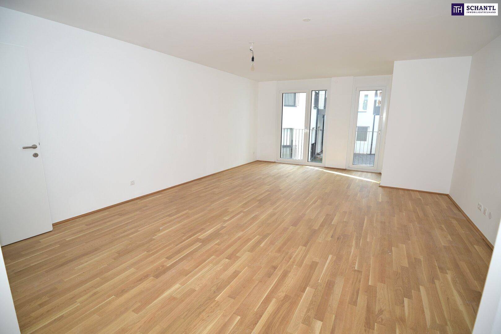 Heller Wohnraum mit hellem Parkettboden und Glastüren, die zu einem kleinen Balkon führen.