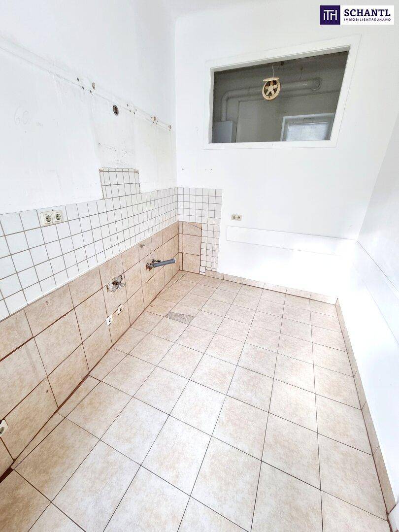 Leere Küche mit Fliesenboden und Wandfliesen, vorbereitet für die Installation neuer Küchenmöbel.
