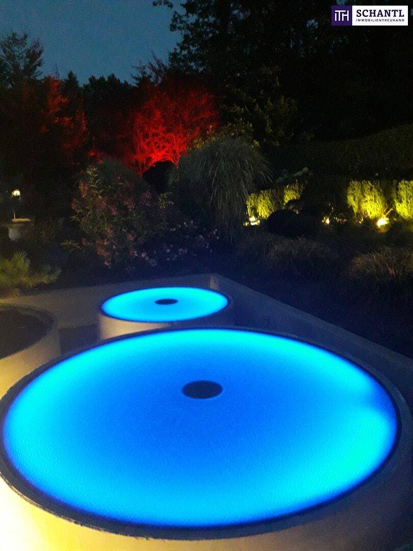 Garten bei Nacht mit stimmungsvoller Beleuchtung und leuchtenden Wasserspielen.