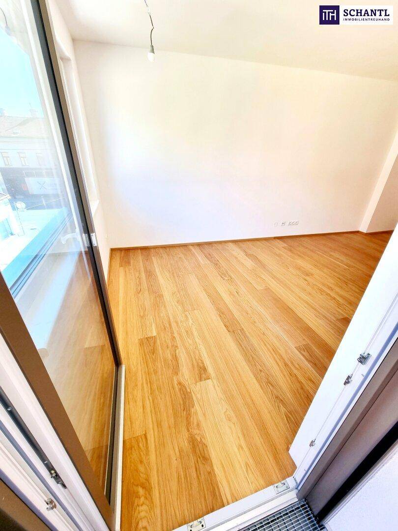 Heller Raum mit Holzboden und Zugang zu einem Balkon oder einer kleinen Terrasse.