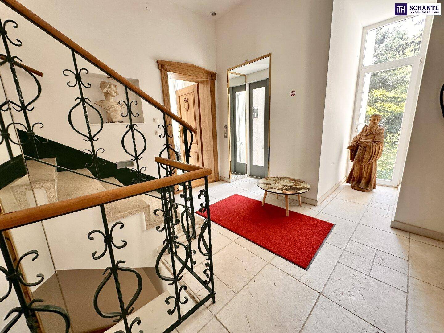 Eingangsbereich mit geschwungener Treppe, Fliesenboden und hohen Fenstern.