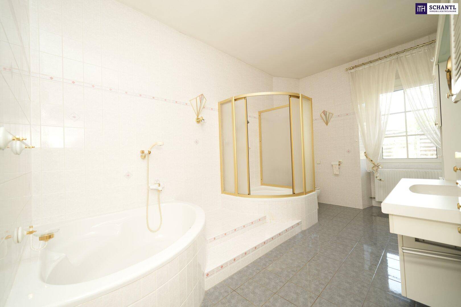 Helles Badezimmer mit Badewanne, Duschkabine und Fenster, ausgestattet mit goldenen Armaturen, sehr gepflegt.