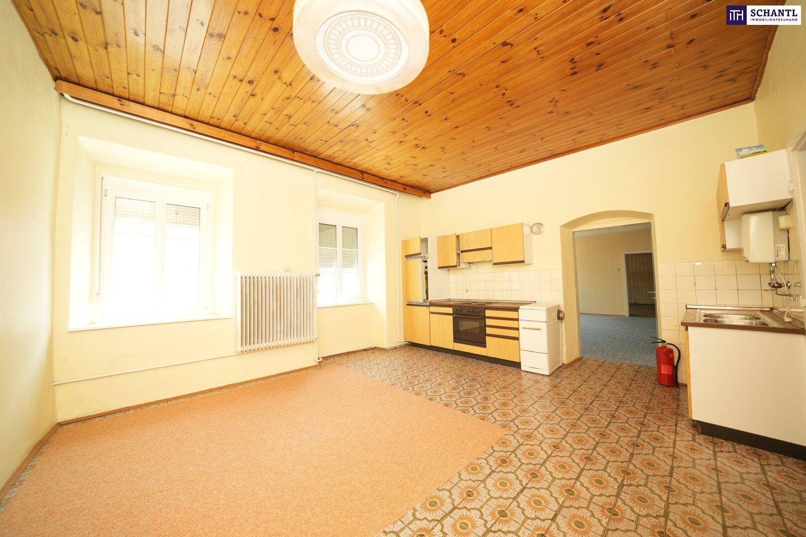 Küche mit Holzdecke, Fliesenboden und einfacher Einbauküche, hell durch große Fenster, benötigt Modernisierung.