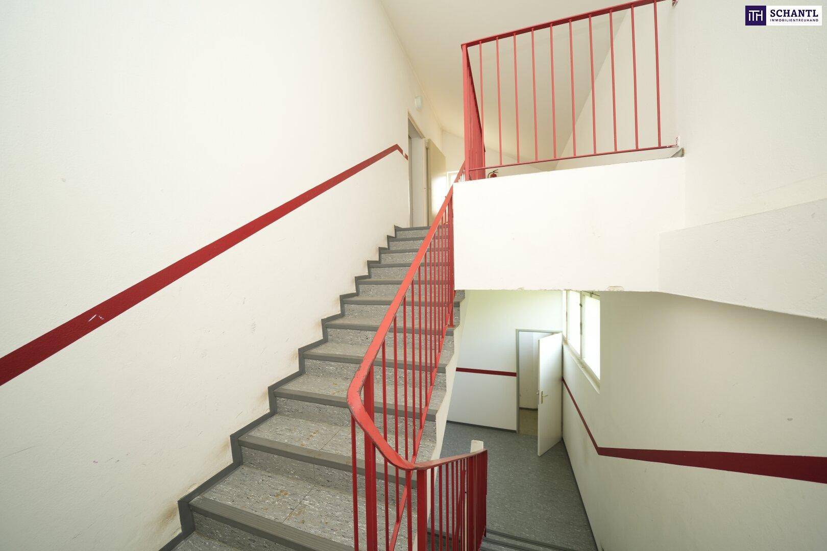 Helles Treppenhaus mit Steinstufen und rotem Geländer, führt zu verschiedenen Etagen, gut erhalten.