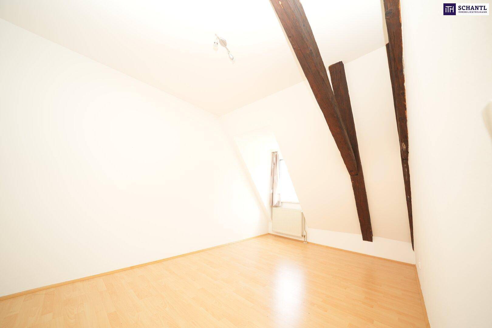 Helles Zimmer mit Laminatboden, Dachschräge und sichtbaren Holzbalken, gemütlich und funktional eingerichtet.