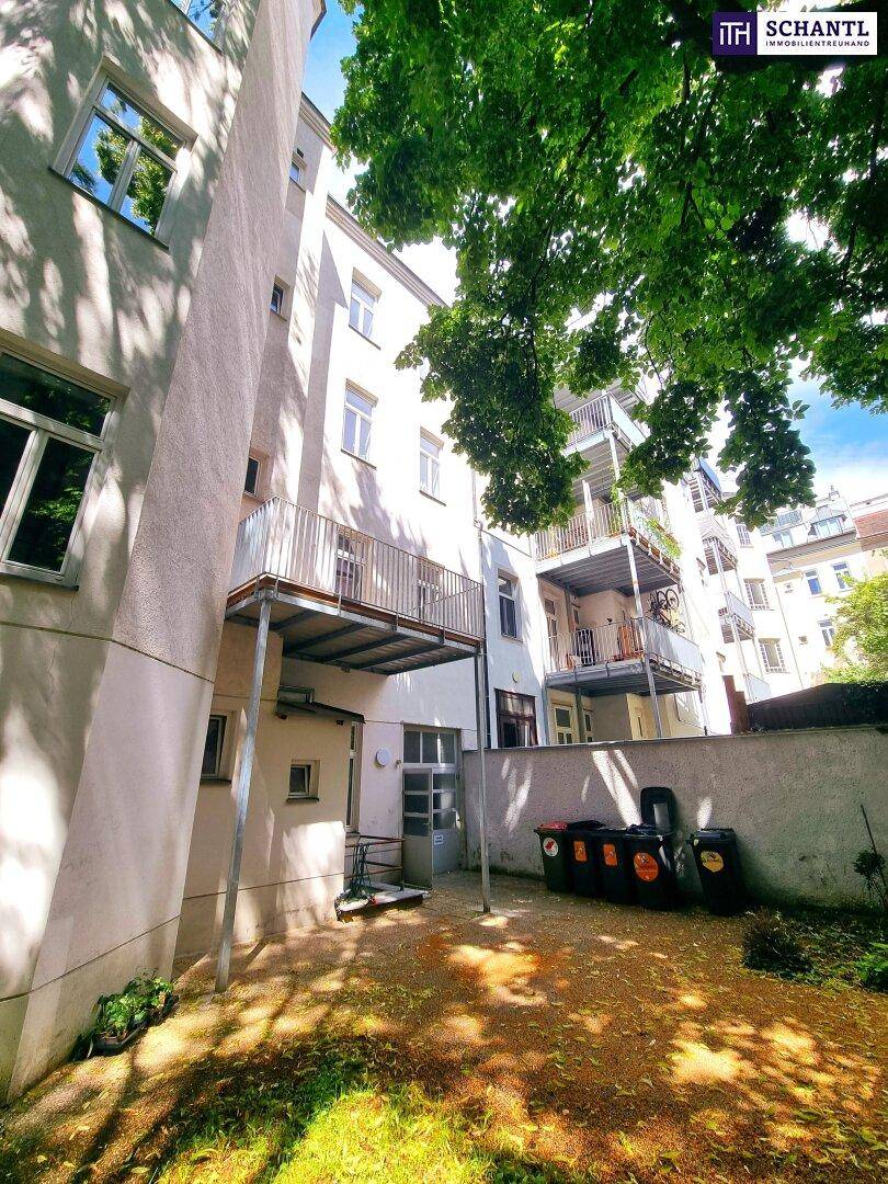 Rückansicht eines Altbaus mit Balkonen und einem begrünten Innenhof, der Mülltonnen beherbergt.