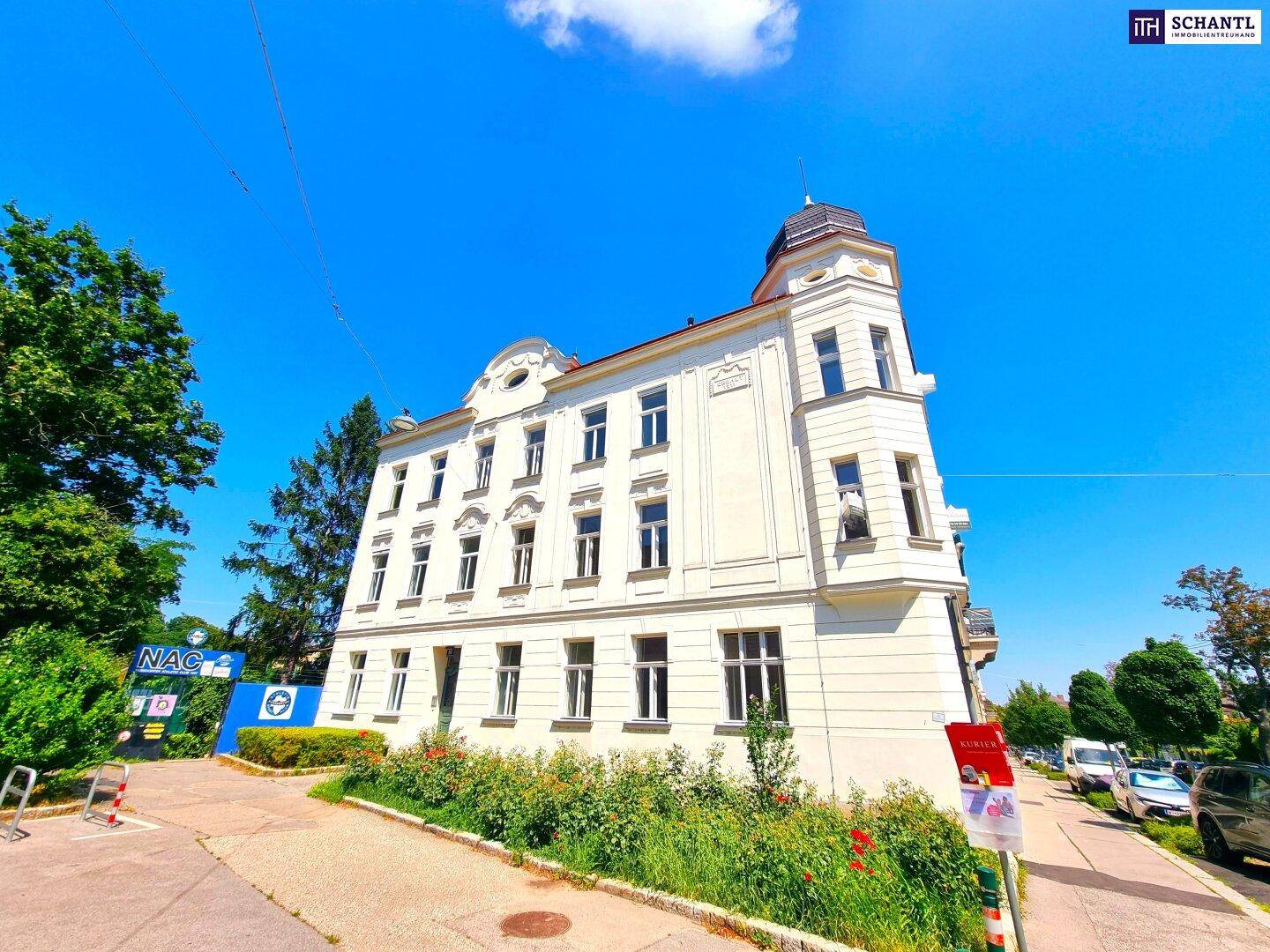 Historisches Eckgebäude mit klassischer Fassade und blühenden Pflanzen im Vorgarten.