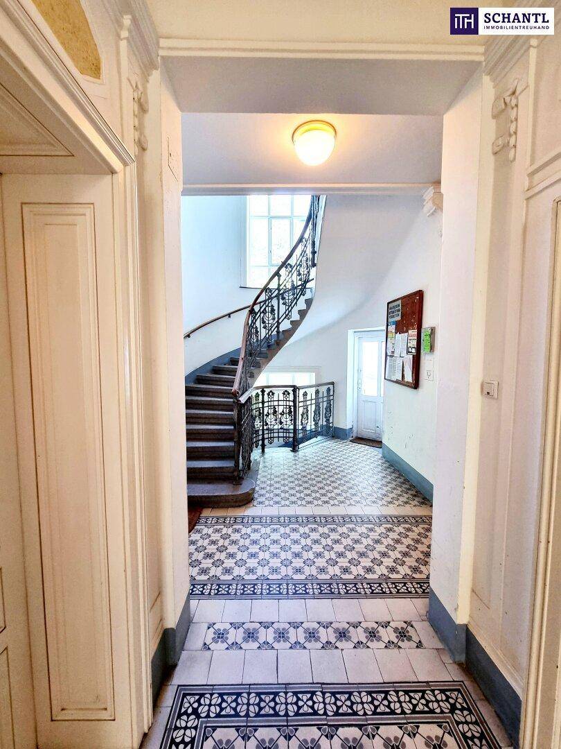 Historisches Treppenhaus mit kunstvollem Geländer und gemustertem Fliesenboden.