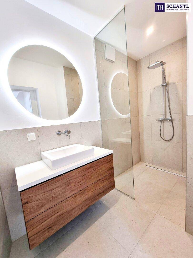 Elegantes Badezimmer mit Einzelwaschbecken, rundem Leuchtspiegel und geräumiger begehbarer Dusche.