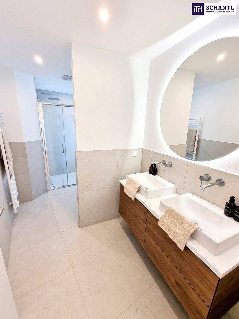 Modernes Badezimmer mit Doppelwaschbecken, beleuchtetem Spiegel und begehbarer Dusche.