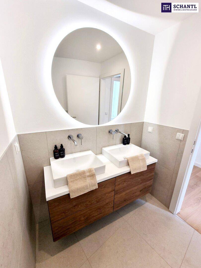Modernes Badezimmer mit Doppelwaschbecken, beleuchtetem Spiegel und Holzunterschrank.