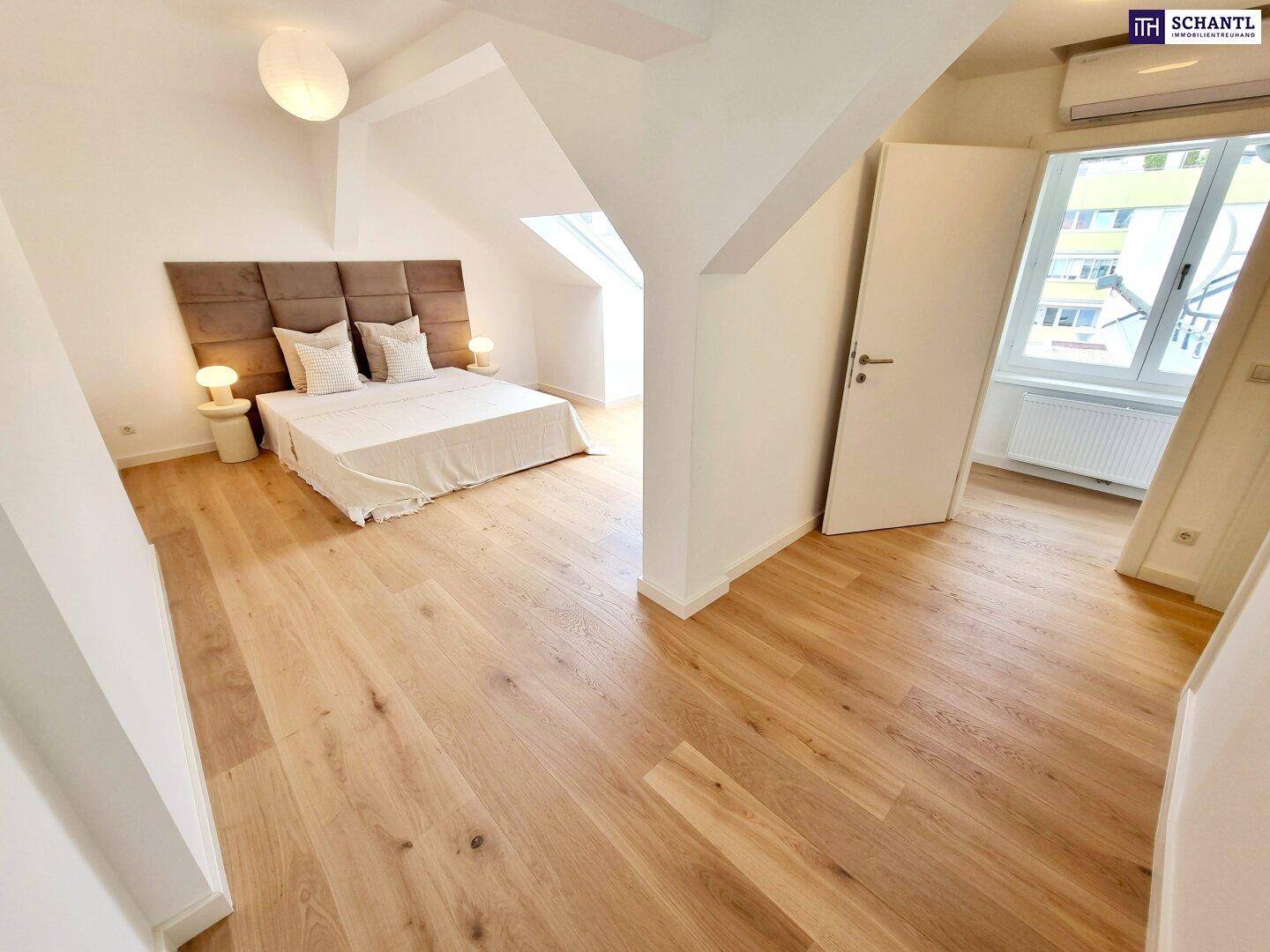 Modernes Schlafzimmer mit Holzboden, gepolstertem Kopfteil und Zugang zu einem weiteren Raum.
