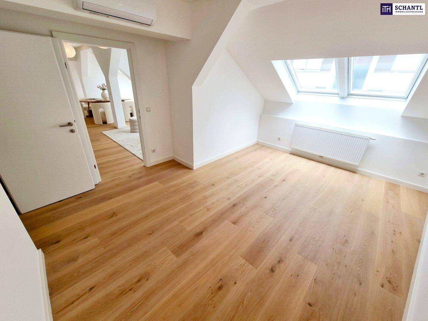 Geräumiges, unmöbliertes Schlafzimmer mit Holzboden, Dachfenstern und Heizkörper.