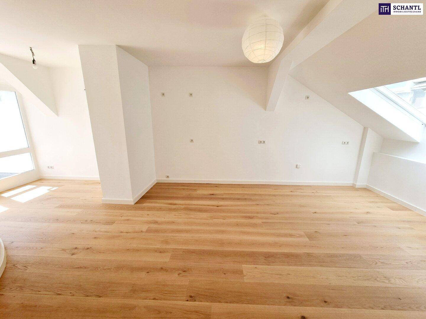 Heller, leerer Raum im Dachgeschoss mit hellem Holzplankenboden und schrägen Decken mit Dachfenstern.