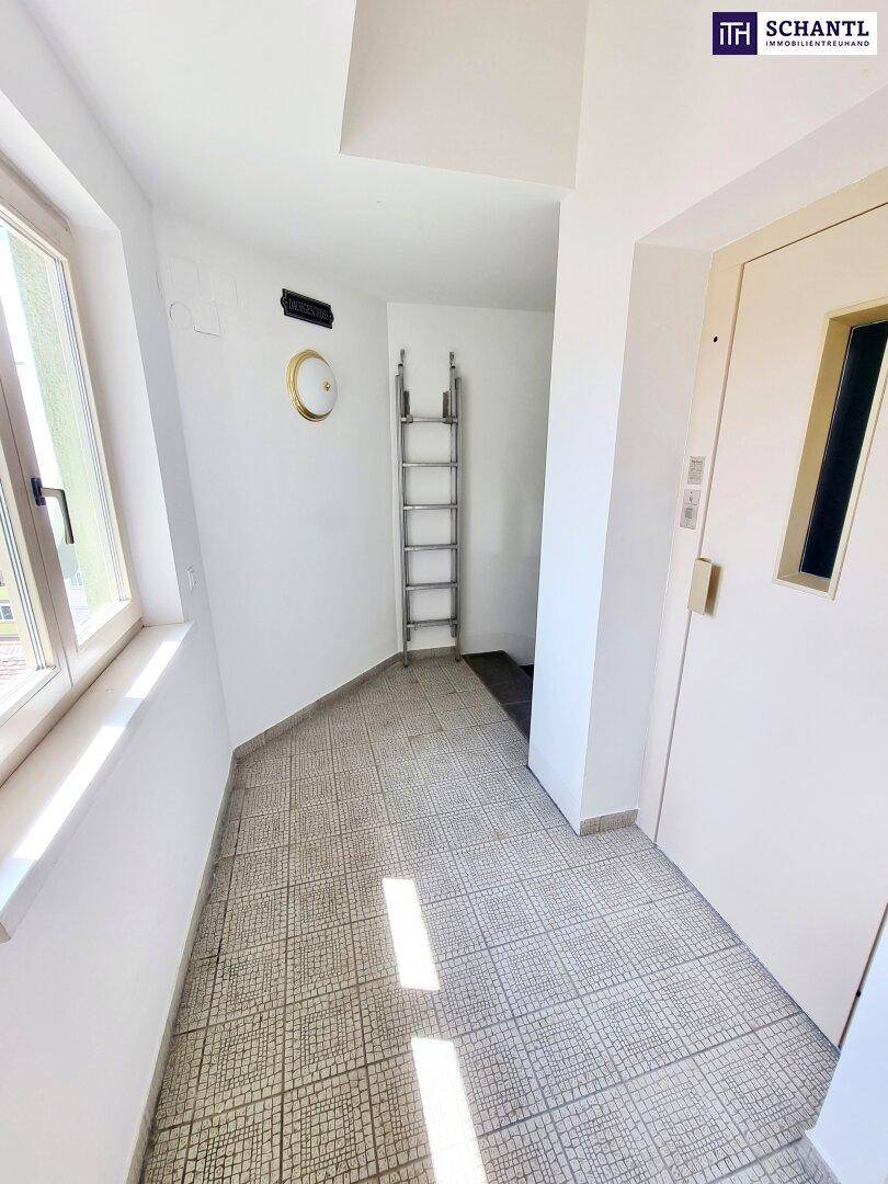 Heller Flur mit Fliesenboden, einem Fenster und einer Aufzugstür, die Zugang zu den oberen Etagen bietet.