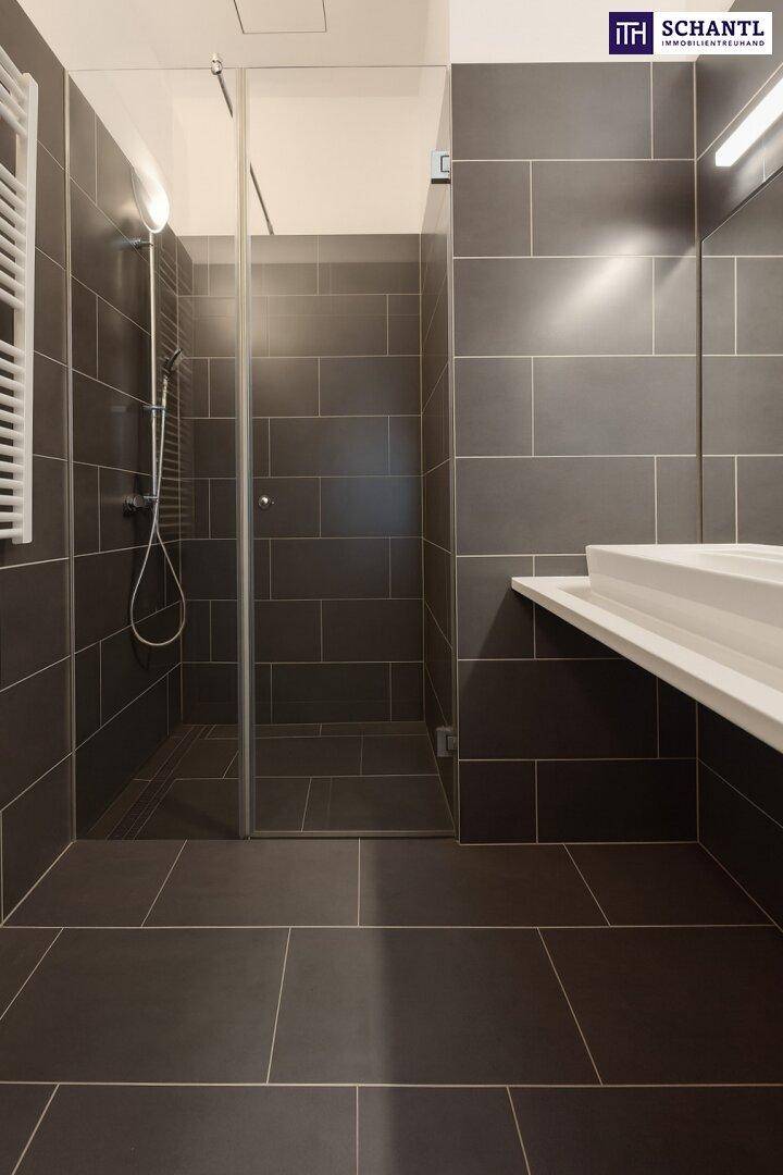Modernes Badezimmer mit großen grauen Fliesen, ebenerdiger Dusche und beheiztem Handtuchhalter.