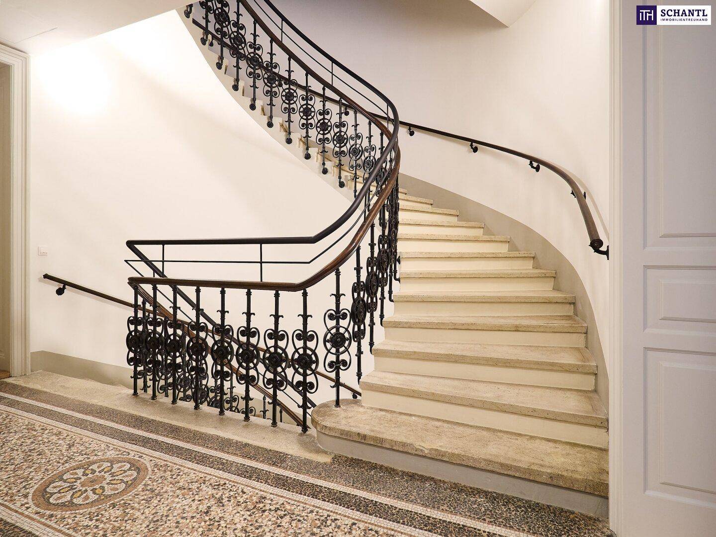 Geräumiges Treppenhaus mit geschwungener Treppe, schmiedeeisernem Geländer und dekorativem Mosaikboden.