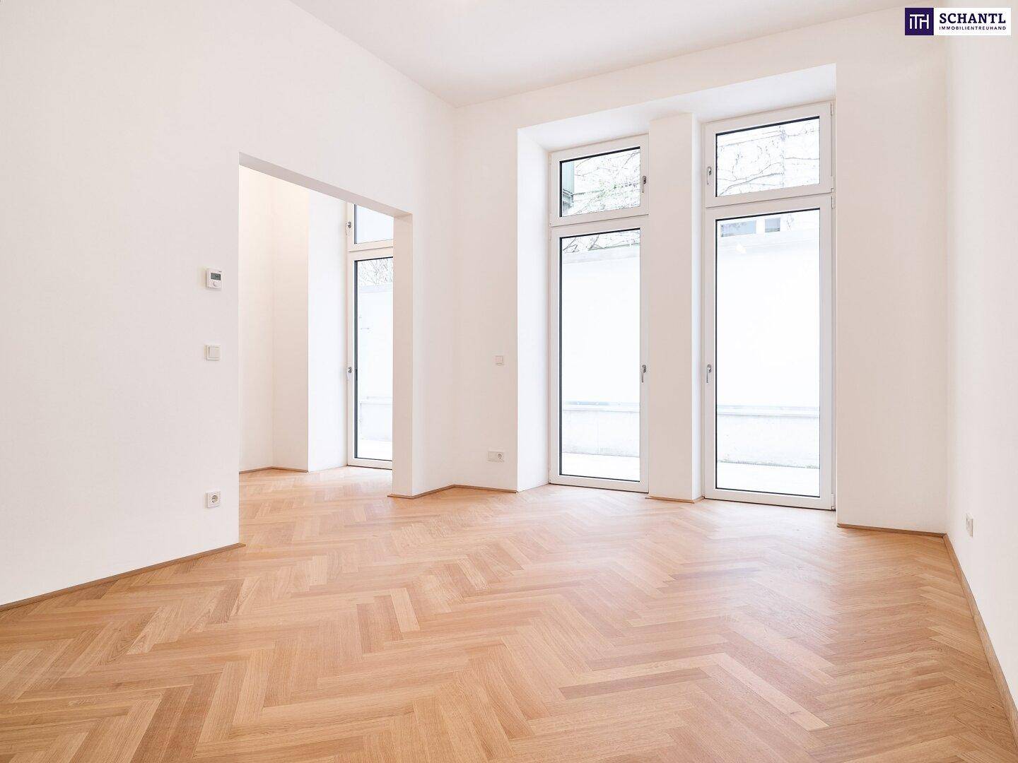 Heller, leerer Raum mit elegantem Fischgrätparkett und hohen Fenstern, die viel Tageslicht hereinlassen.