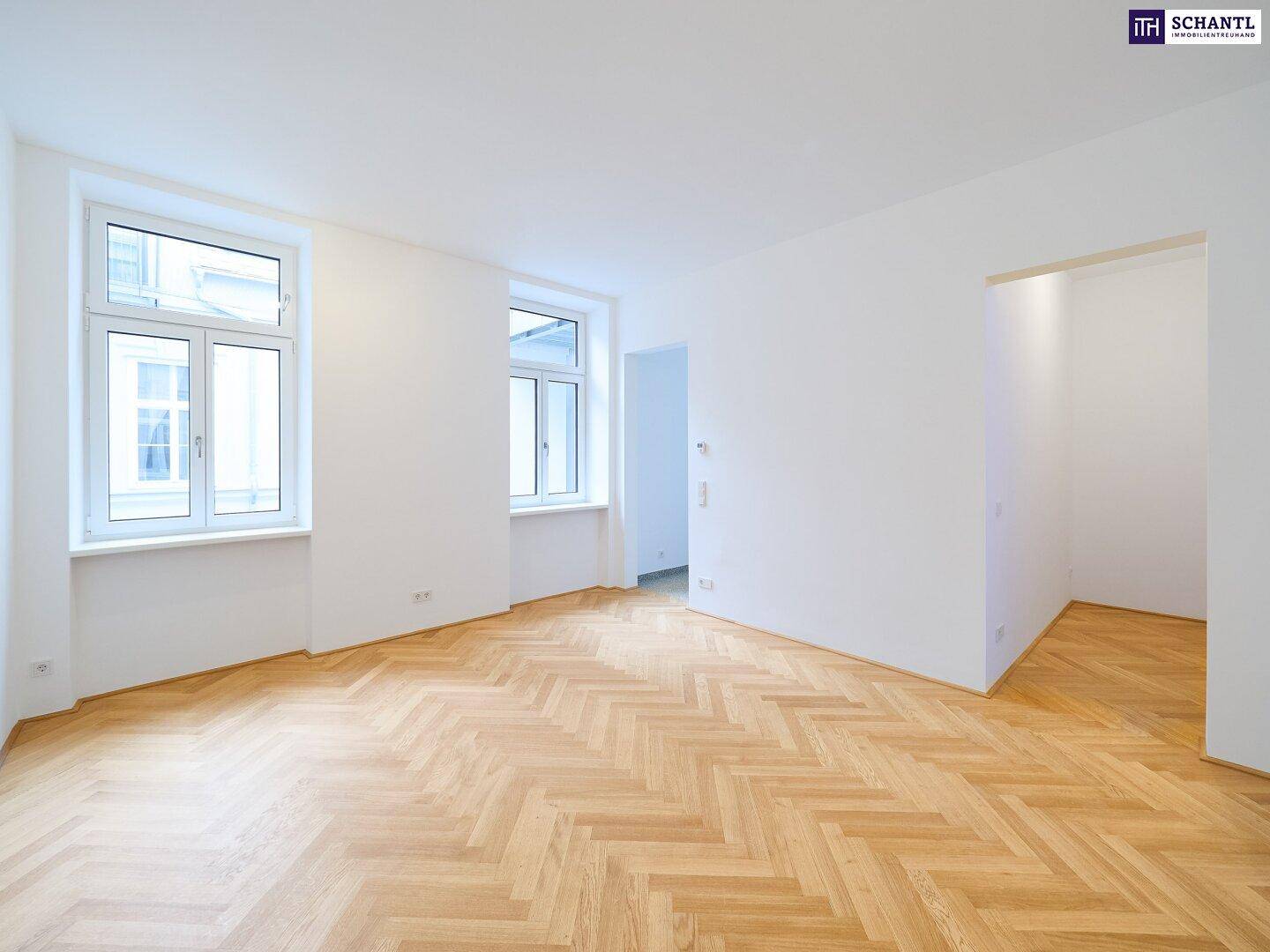 Heller Wohnraum mit elegantem Fischgrätparkett und großen Fenstern, die den Raum erhellen.