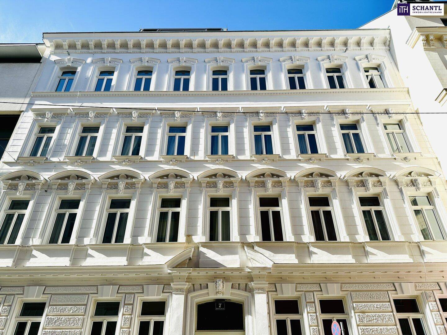 Elegante weiße Fassade eines historischen Gebäudes mit zahlreichen Fenstern und architektonischen Verzierungen.