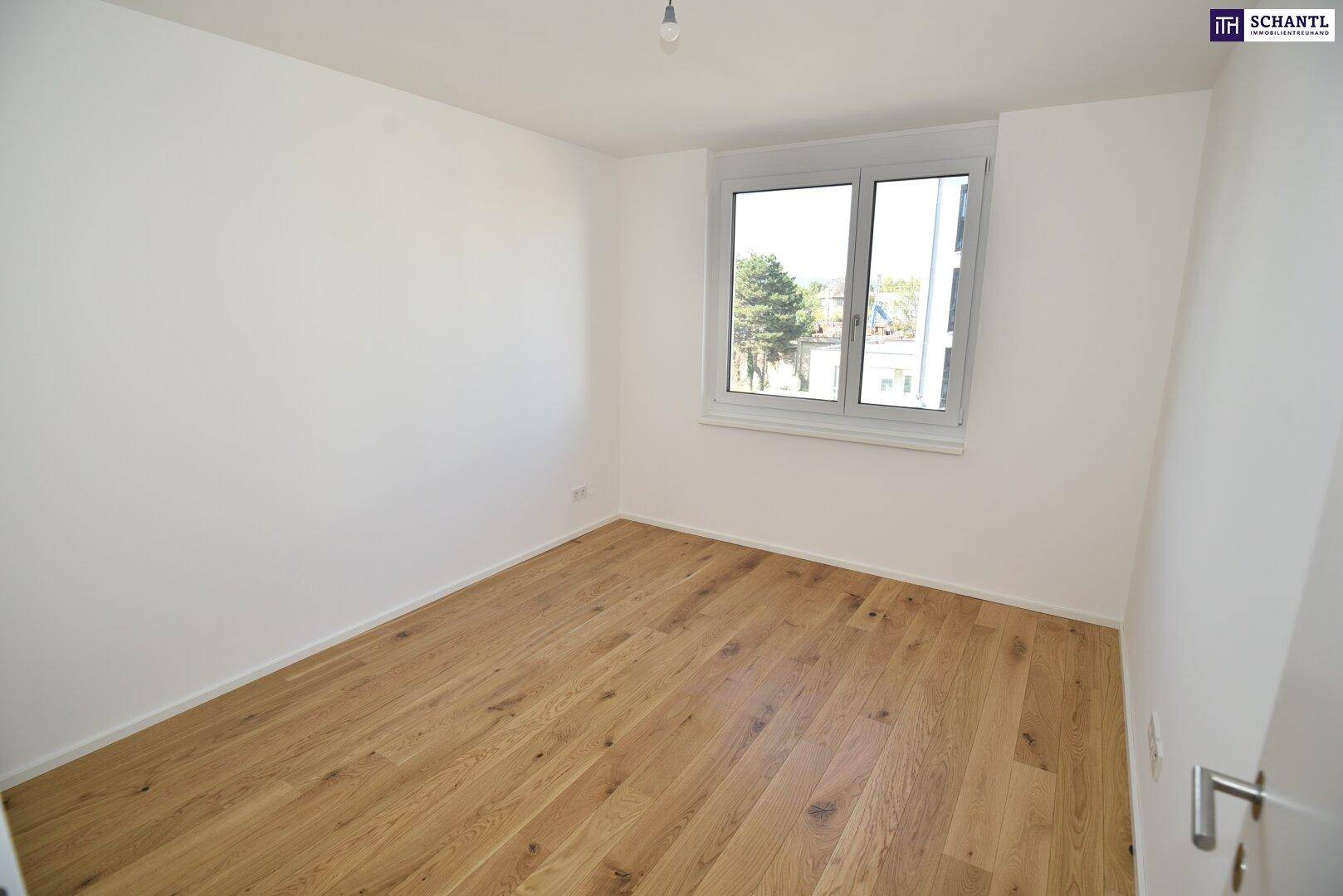 Helles Schlafzimmer mit Holzboden und einem Fenster, das einen Blick ins Grüne ermöglicht.