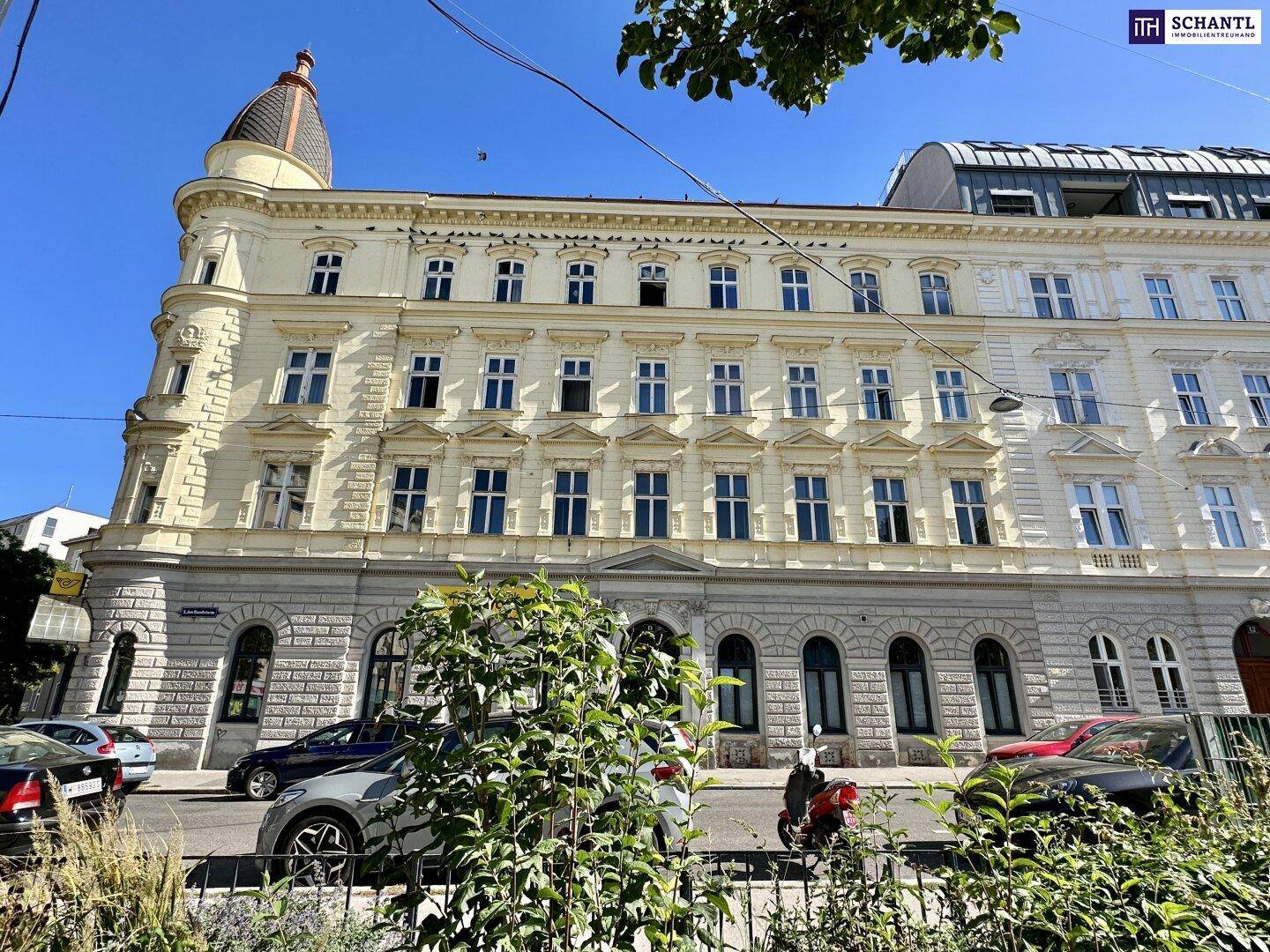 Klassische Fassade eines Altbaus mit vielen Fenstern und einem belebten Straßenbereich davor.