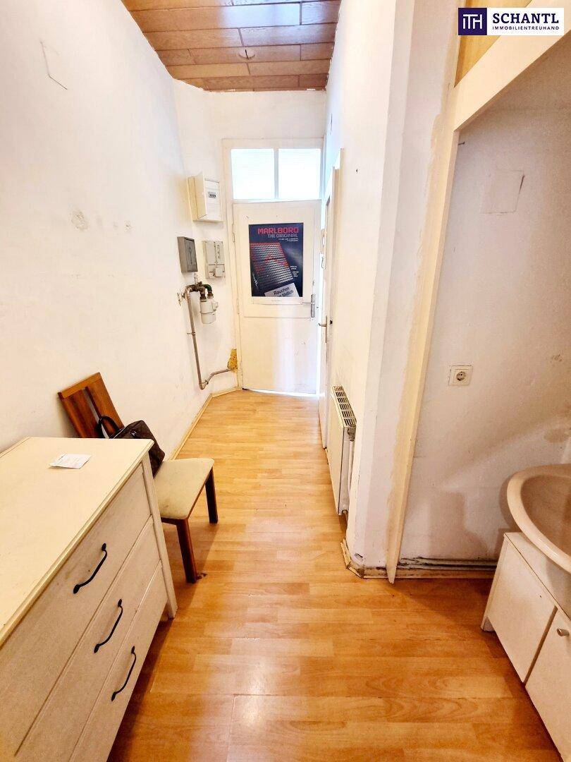 Schmaler Flur mit Holzparkett und einfacher Einrichtung, der zum Eingangsbereich führt.
