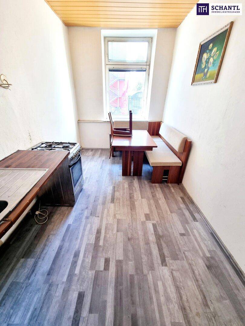 Einfache Küche mit Esstisch, Holzbank und älterem Gasherd, bereit zur Modernisierung.