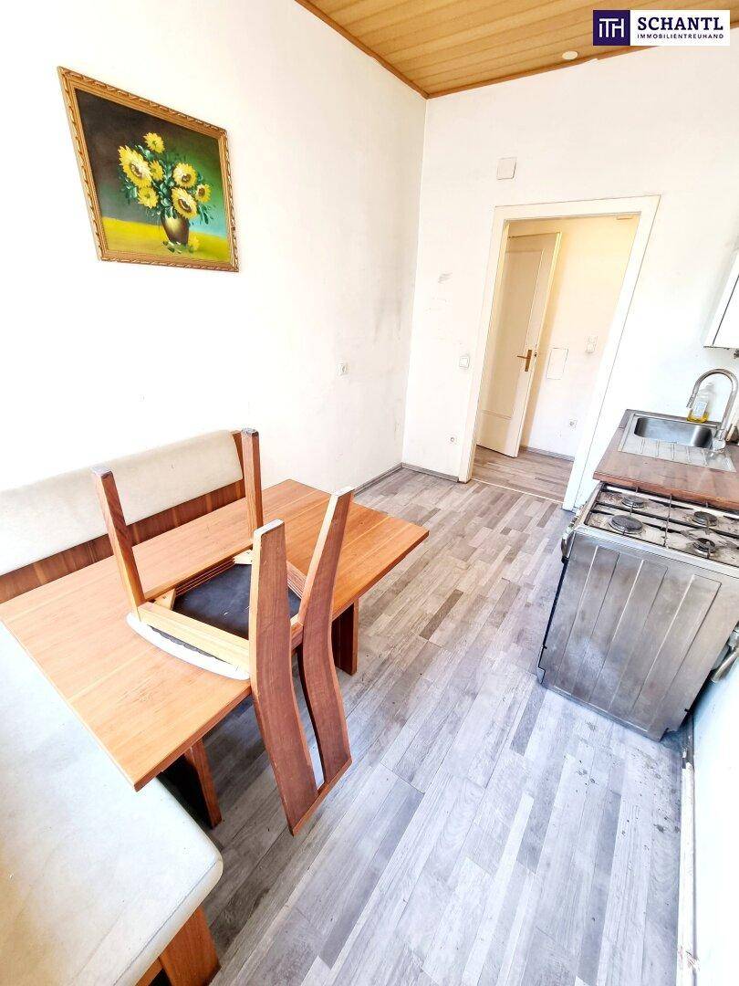 Einfache Küche mit Esstisch, Holzbank und älterem Gasherd, bereit zur Modernisierung.