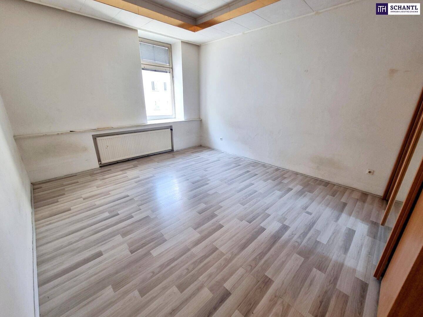 Unmöbliertes Zimmer mit Laminatboden und Fenster, das auf die Straße blickt.