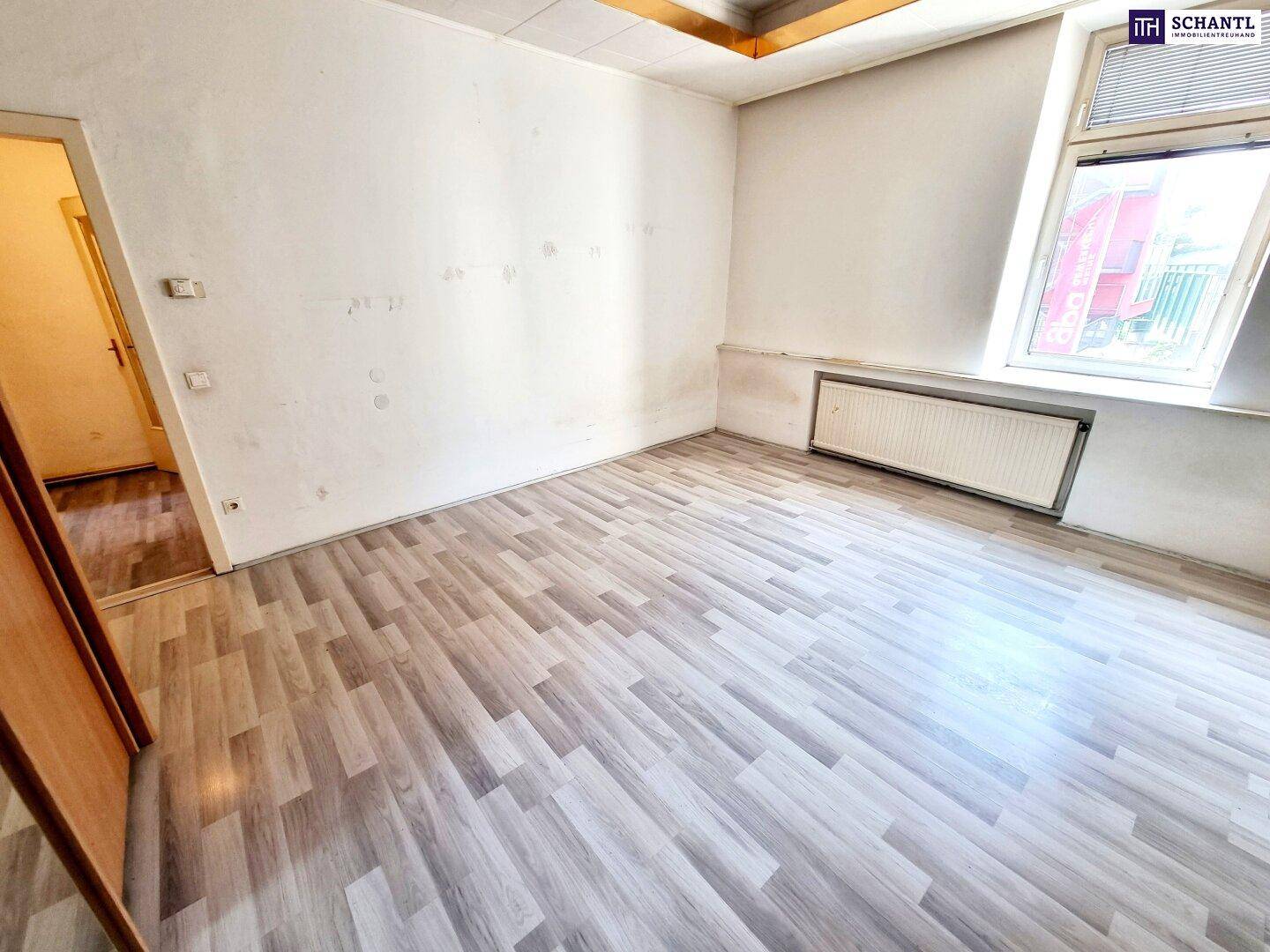 Unmöbliertes Zimmer mit Laminatboden und Heizkörper unter dem Fenster, bereit zur Renovierung.