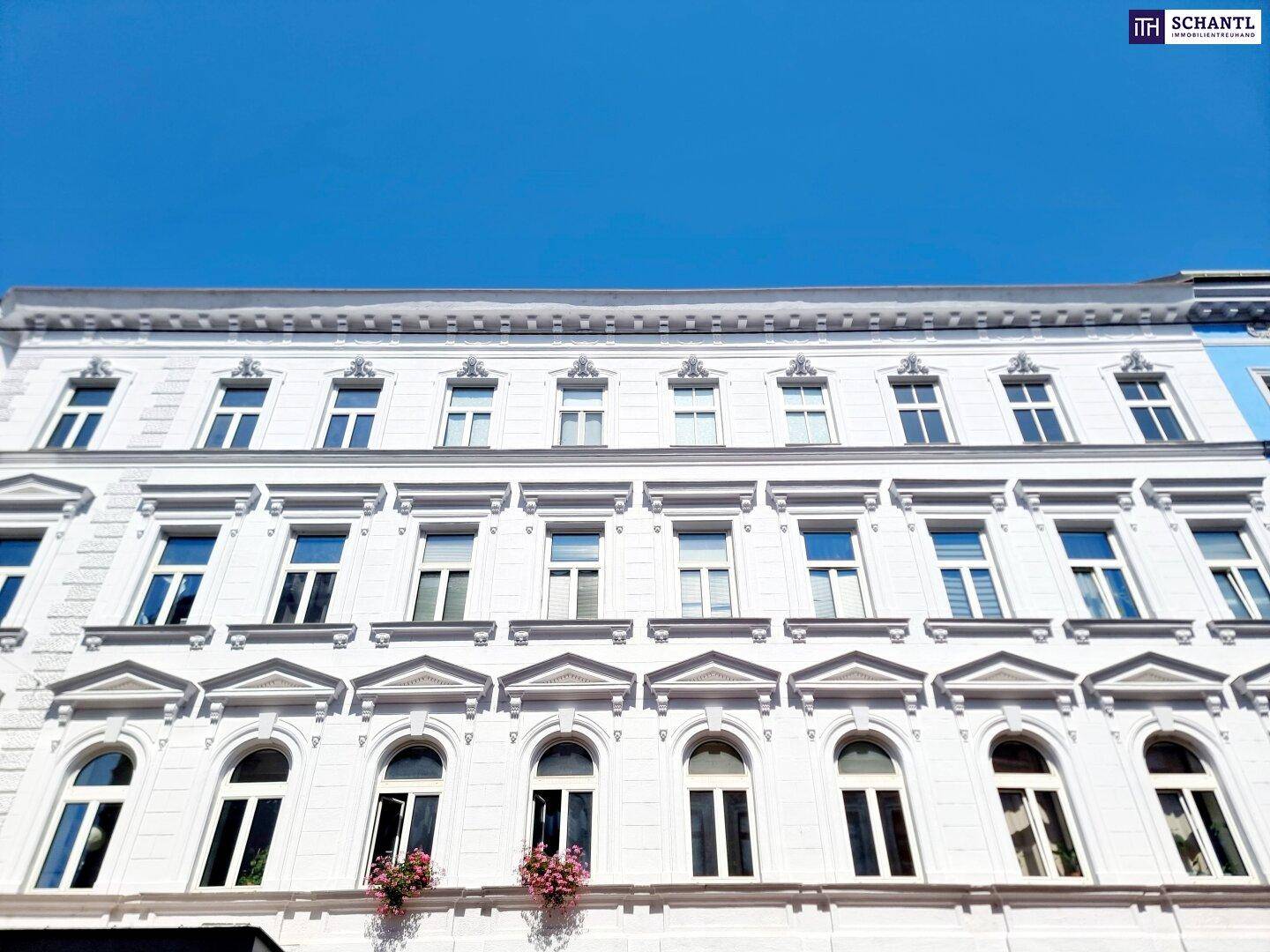 Historische Fassade eines Altbaus mit vielen Fenstern und dekorativen Elementen unter blauem Himmel.