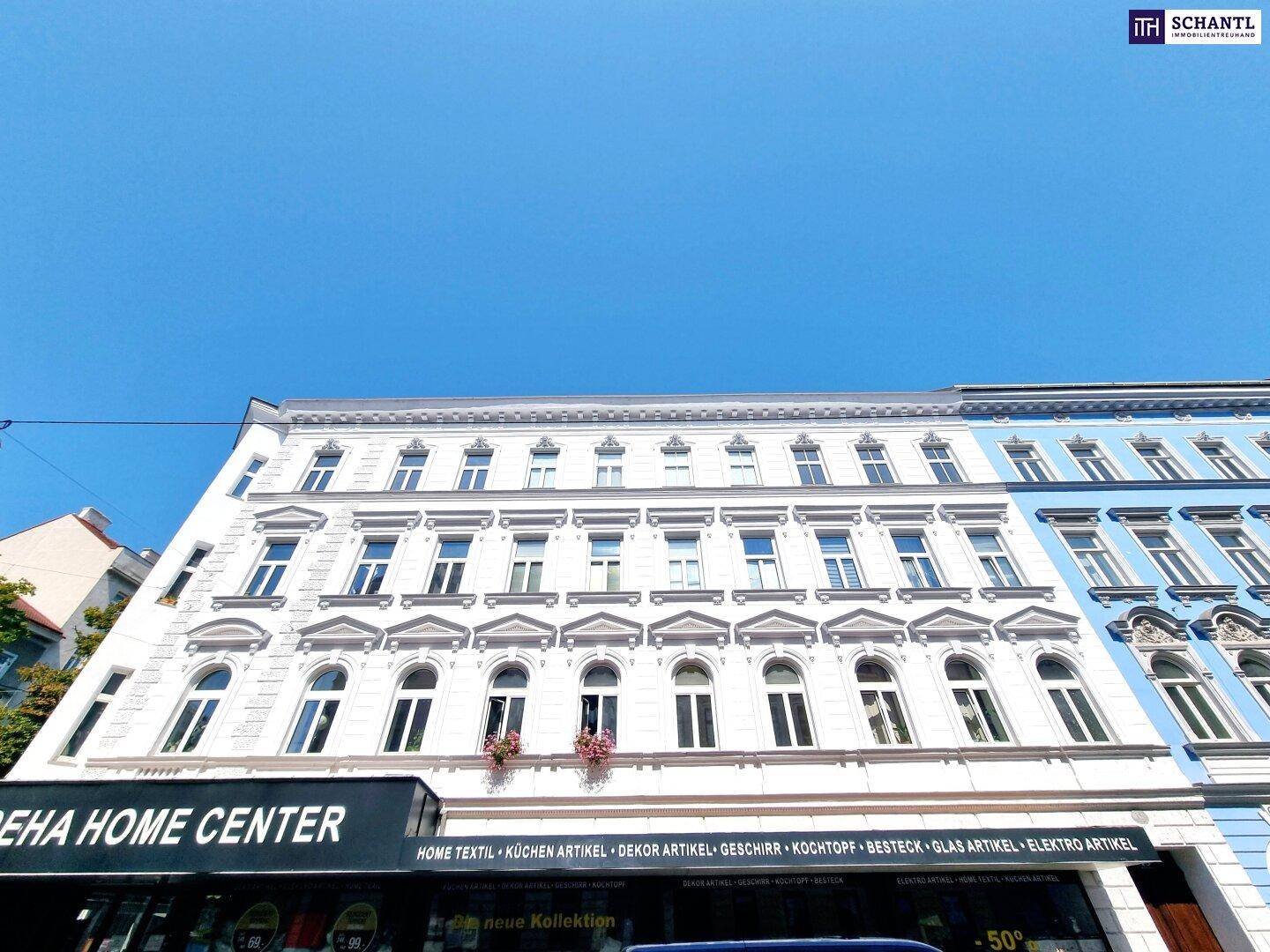 Historische Fassade eines Altbaus mit vielen Fenstern und dekorativen Elementen unter blauem Himmel.