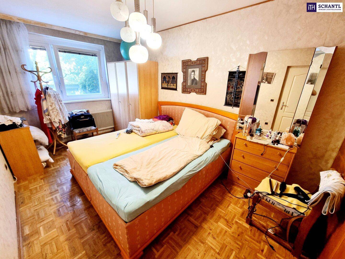 Schlafzimmer mit Doppelbett, Parkettboden, großem Spiegel und natürlichem Lichteinfall.