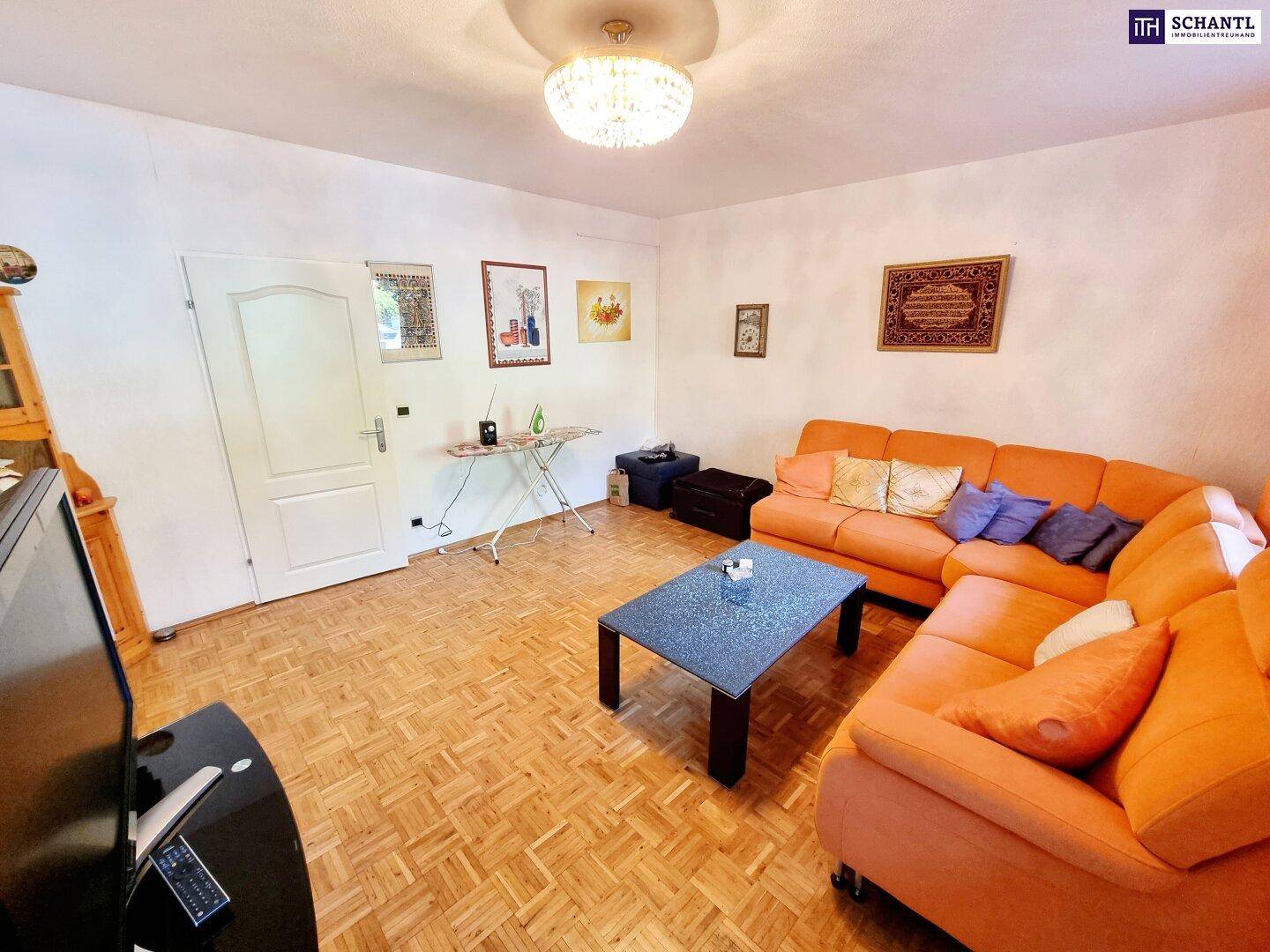 Gemütliches Wohnzimmer mit orangefarbenem Sofa, Parkettboden und schlichter Einrichtung.