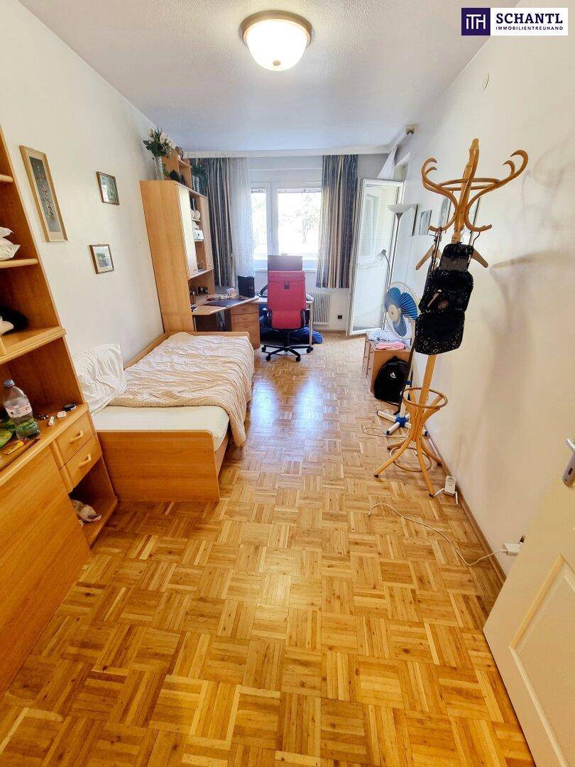 Helles Zimmer mit Einzelbett, Schreibtisch, Parkettboden und großem Fenster.