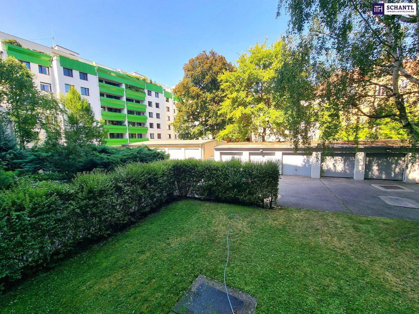 Grüne Außenanlage mit Garagenreihe und Bäumen im Hintergrund, bietet Parkmöglichkeiten.