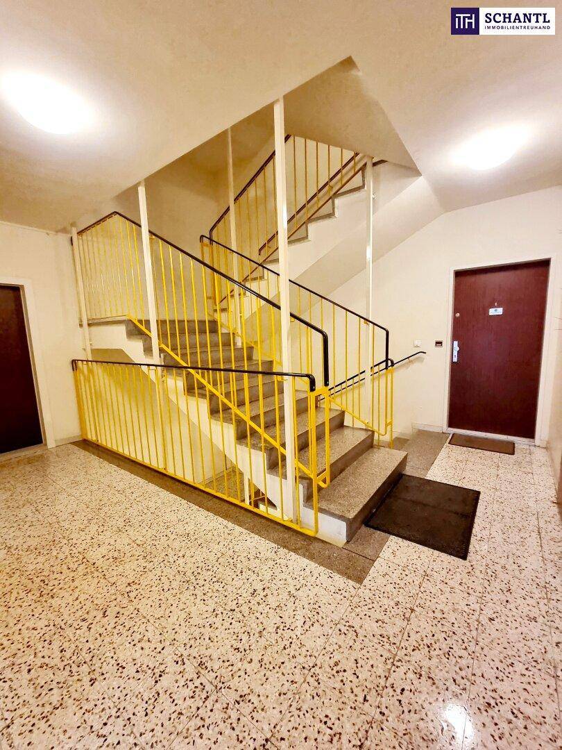 Treppenhaus mit Terrazzoboden, gelbem Geländer und Zugang zu den einzelnen Wohnungen.