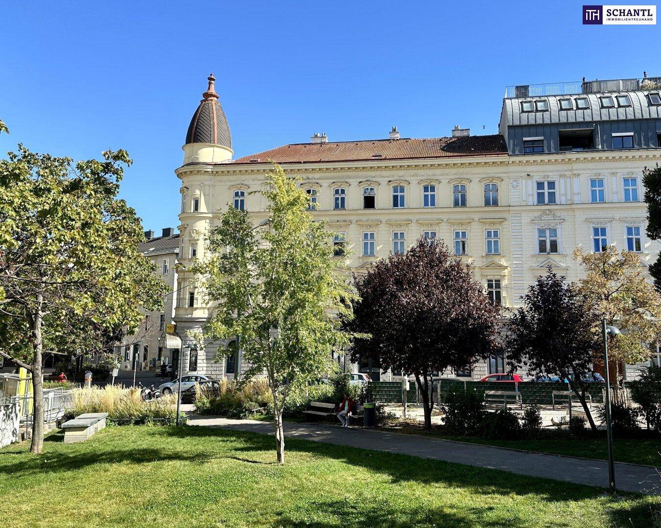 Historisches Gebäude mit Parkanlage im Vordergrund und sonnigem Wetter.