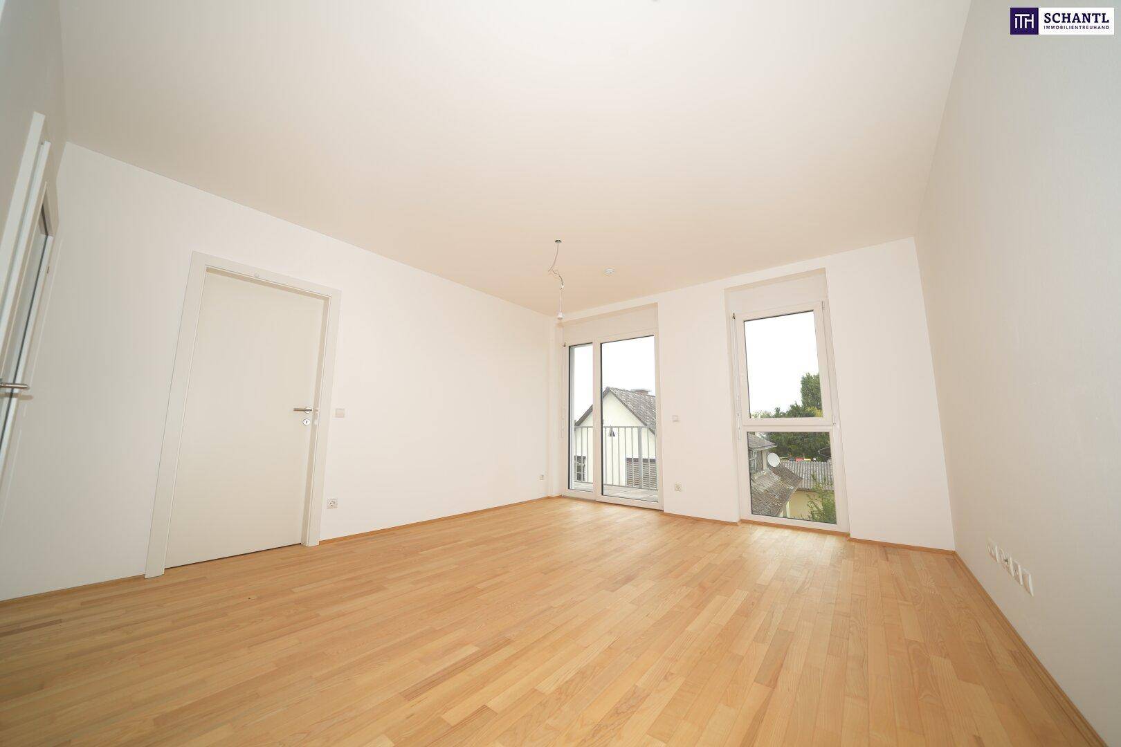 Geräumiges Zimmer mit Holzboden und großen Fenstern, bietet viel Tageslicht und Zugang ins Freie.
