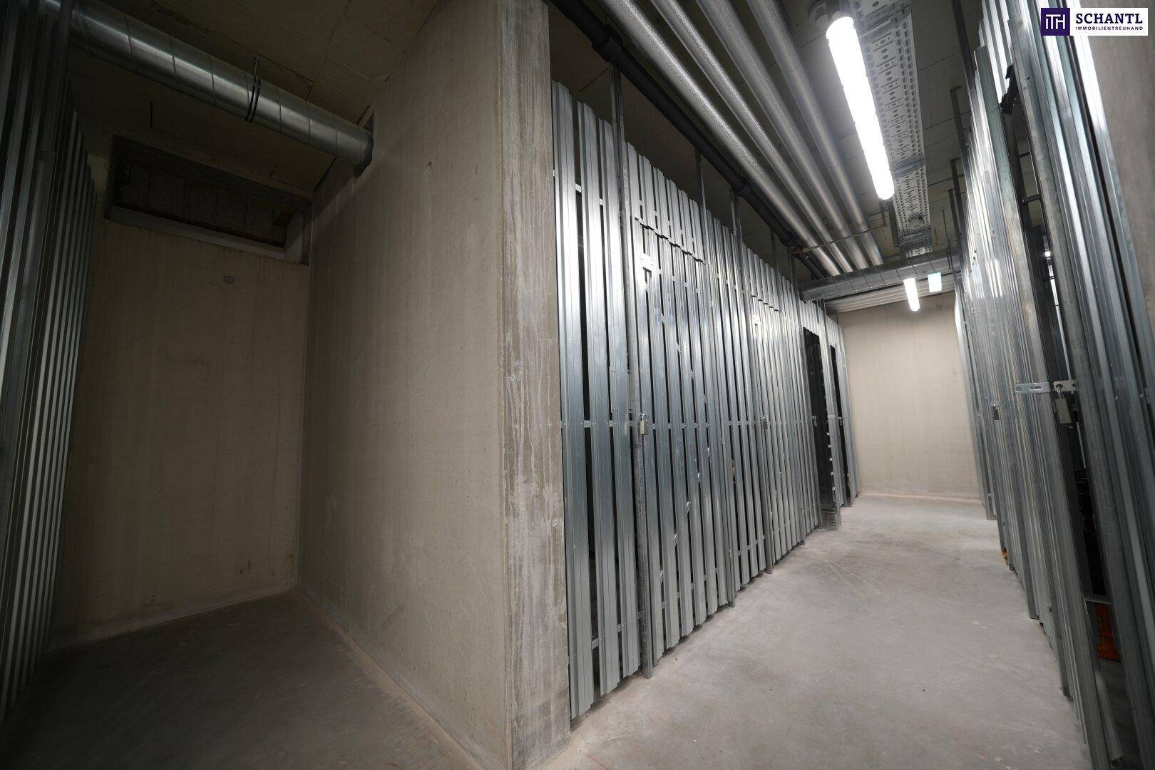 Langer Kellergang mit Metallabtrennungen für individuelle Abstellräume und sichtbaren Leitungen.